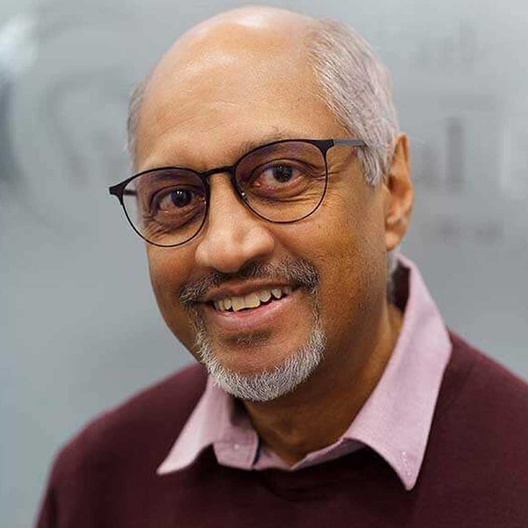 Man wearing glasses and a maroon sweater with a pink shirt underneath, against a gray background