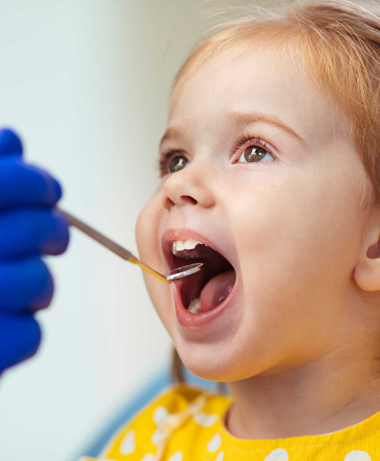 Child at a dental check-up with a gloved hand holding dental tools.