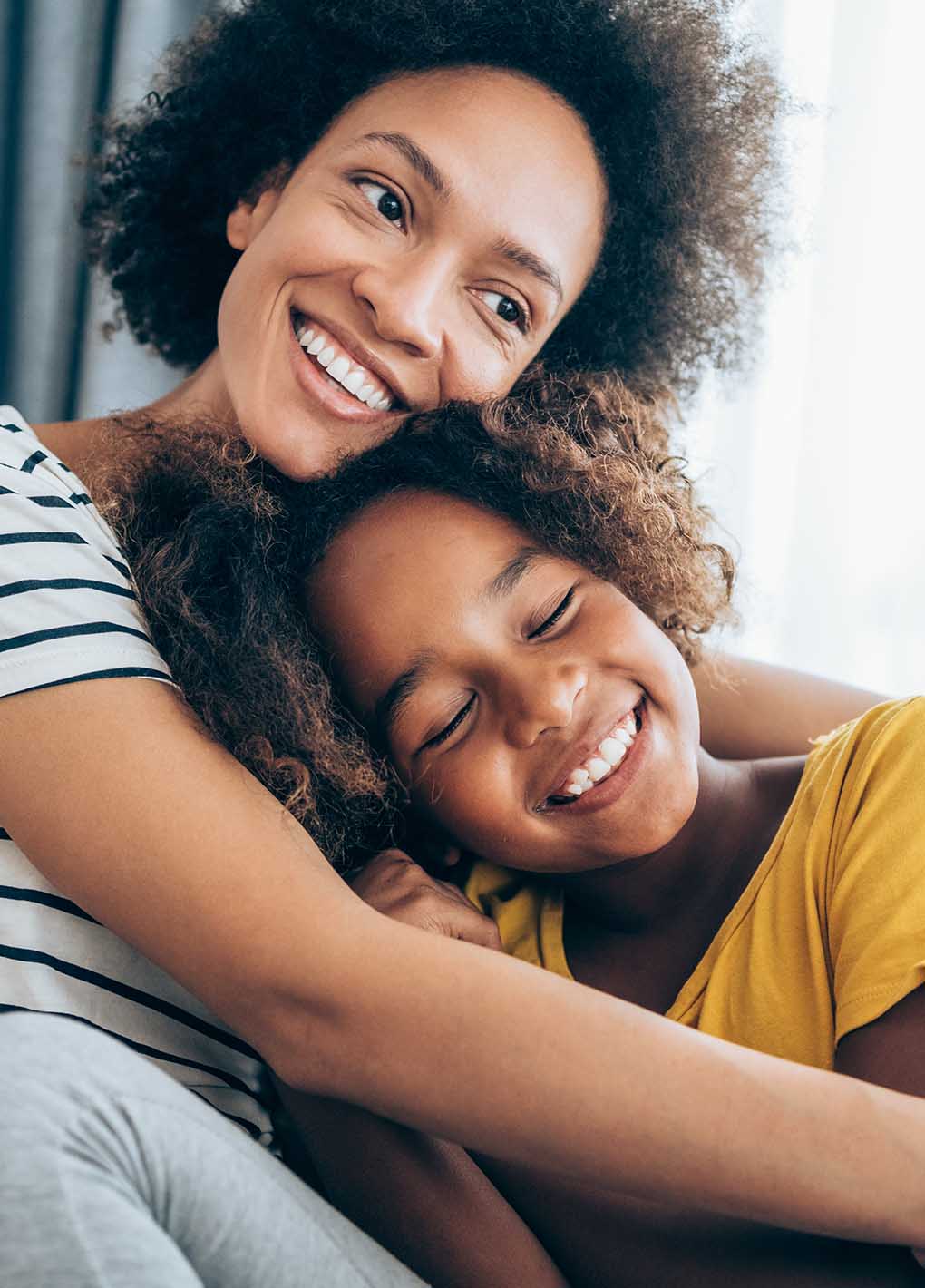 Woman and young girl hugging and smiling indoors