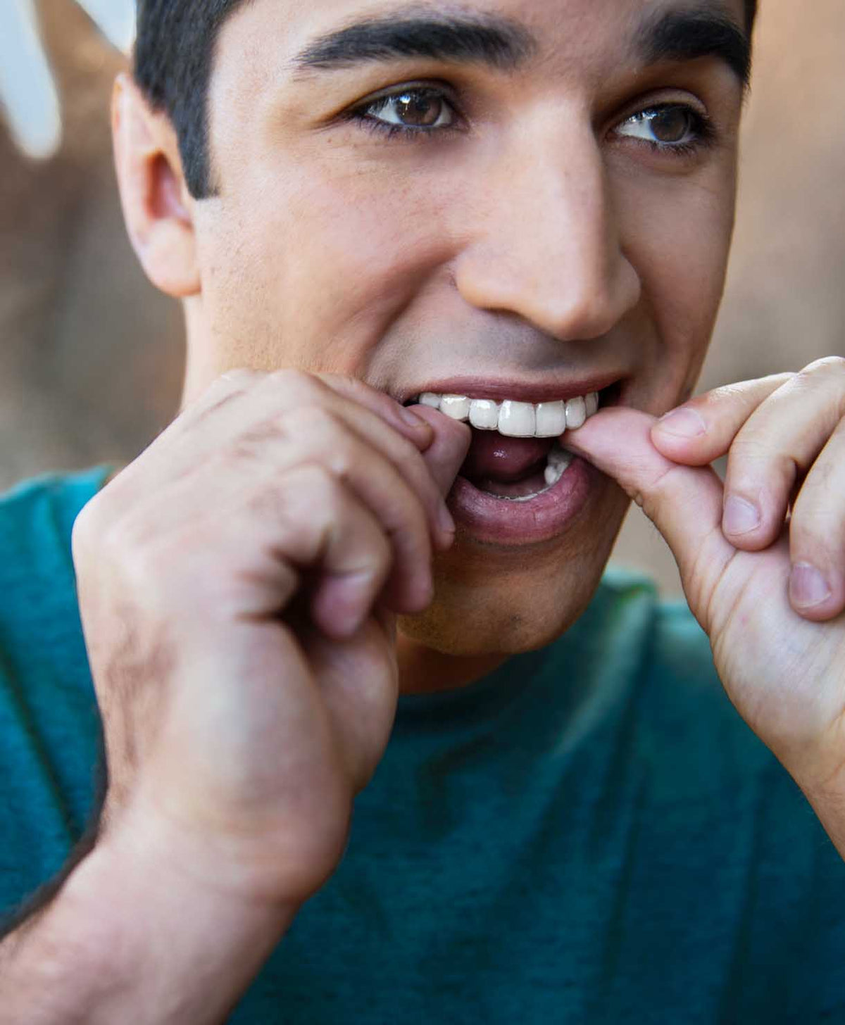 Man with a green shirt biting his fingernail outdoors