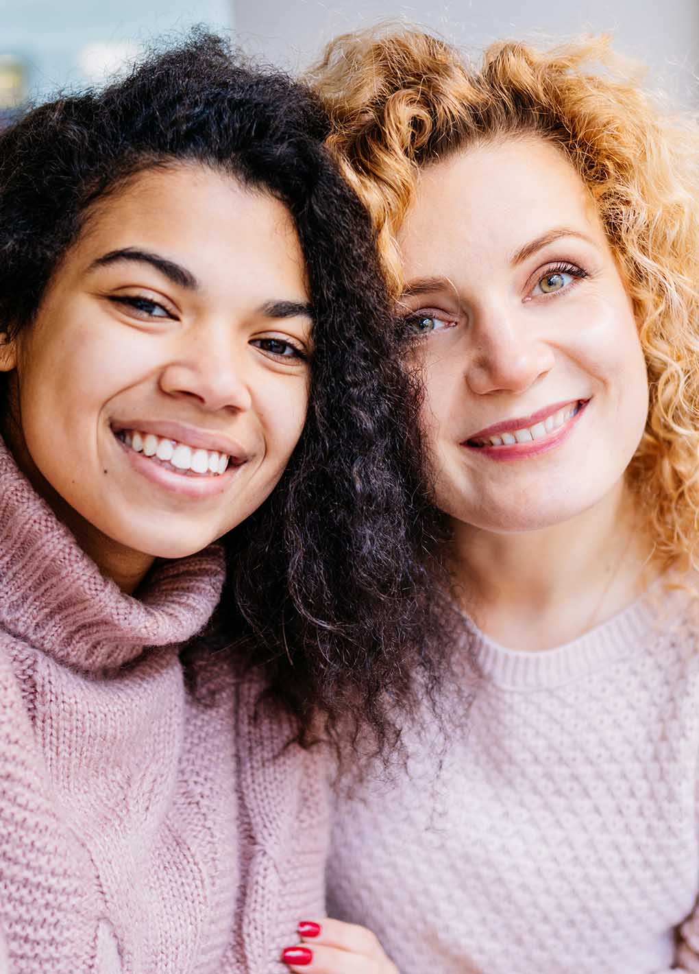 Two women with curly hair smiling close together