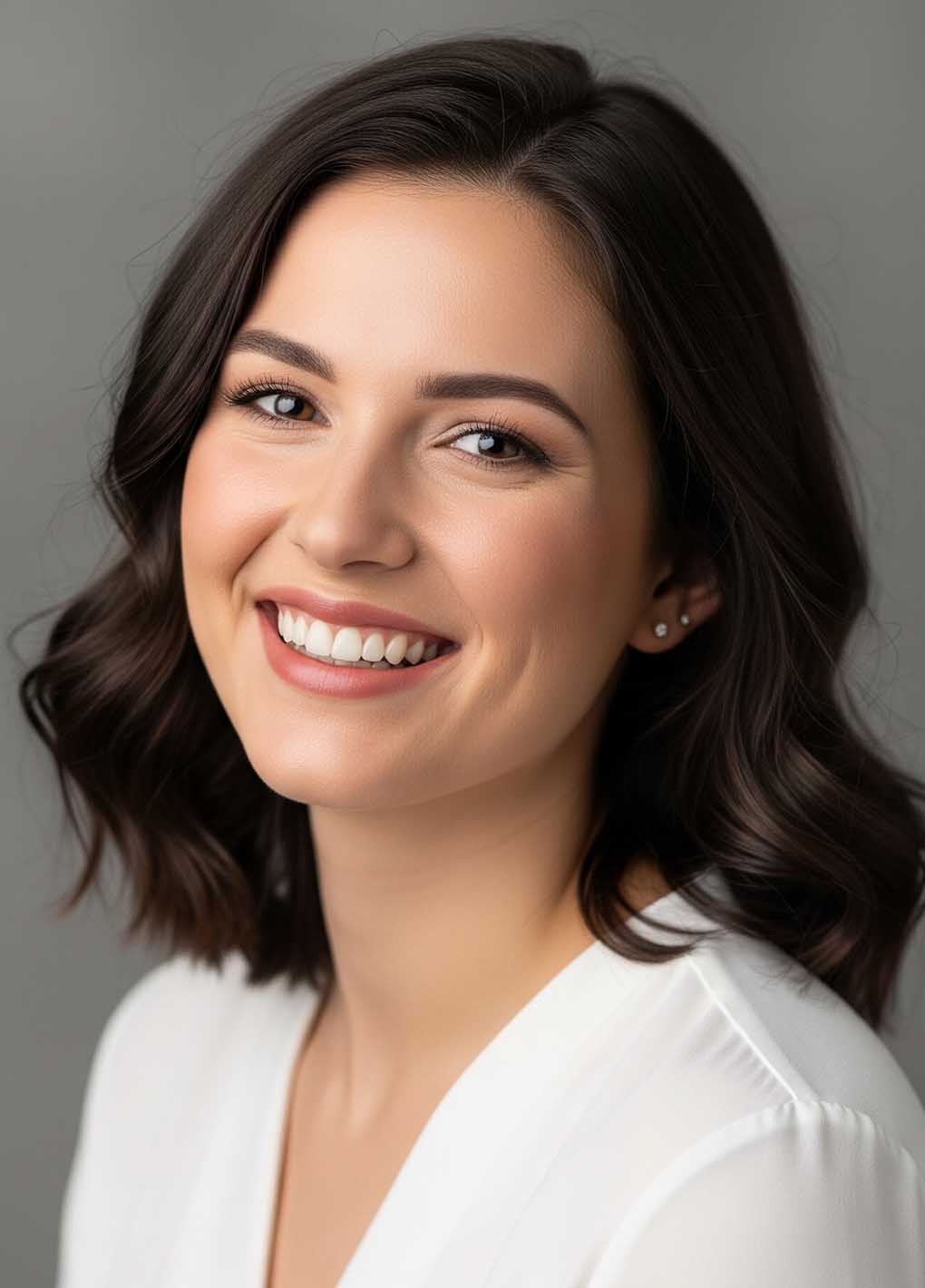 Woman with dark hair and a white shirt against a gray background