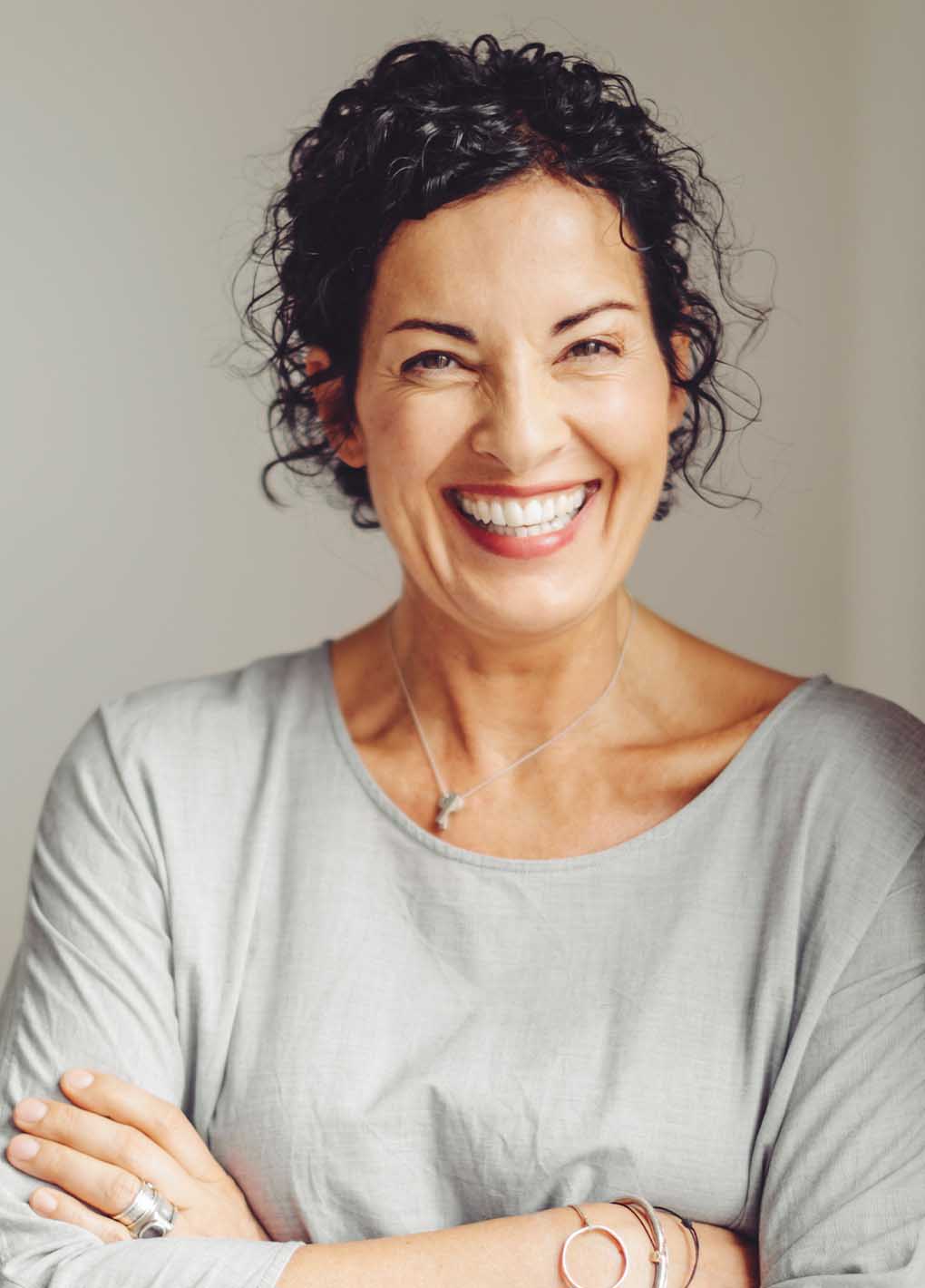 Woman with curly hair wearing a gray shirt against a plain background