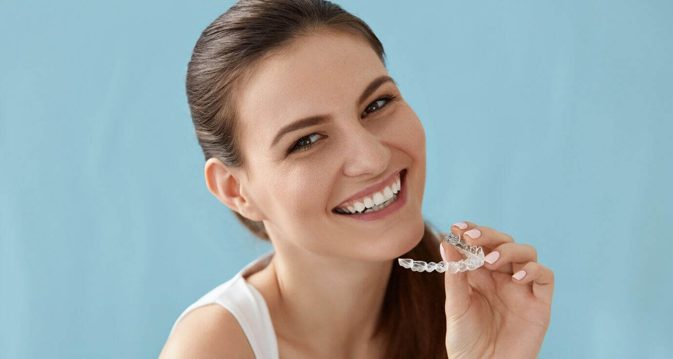 Brunette woman smiling looking forward holding Invisalign clear brace